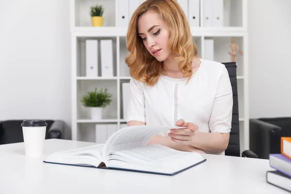 Woman sitting in office with paper coffee cup turning book page with interest. Concept of good reading habits