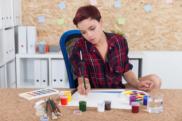 Woman painter at work in college office. Cork board on wall. Palette and paint lie on desk. Concept of higher education in art and sculpture.