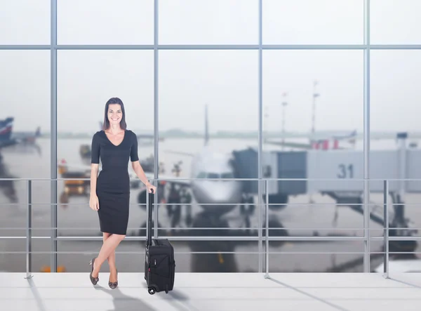 Beautiful girl in black is standing with her suitcase in airport. Concept of travelling and business trips