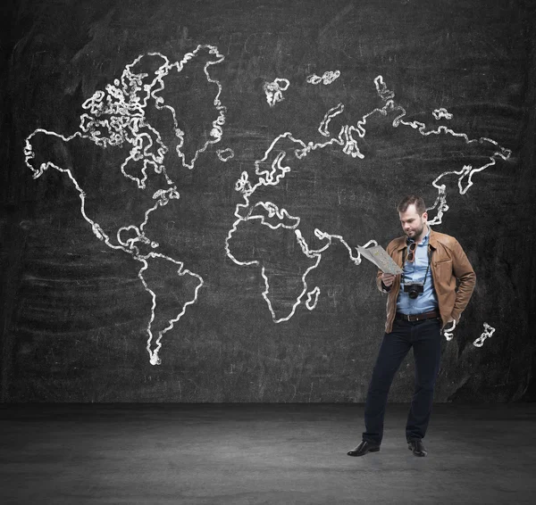 Handsome tourist is examining the map. Black wall with the sketch of the world map.