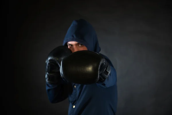 Hooded man in a fighting stance with black boxer gloves.