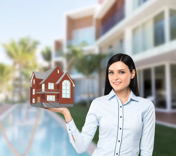 Beautiful brunette property agent presents a new house for sale. Luxury villa in blur as a background.