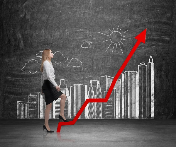 Business woman is going up. Drawn skyscrapers on black chalk board as a growing bar chart and rocketing red arrow.