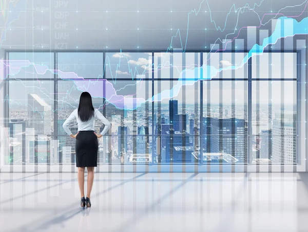 Full-length of brunette lady who is looking through the window. A modern panoramic office with New York city view and forex chart. A concept of the asset management.