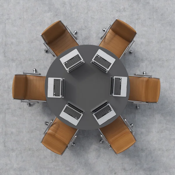 Top view of a conference room. A black round table, six brown leather chairs and six laptops. Office interior. 3D rendering.