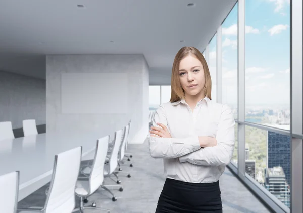 Young beautiful business lady with crossed hands in the panoramic meeting room with huge windows and New York City view.