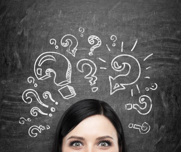 A forehead of the brunette girl who is pondering about unsolved problems. Question marks are drawn around the head. black chalkboard background.