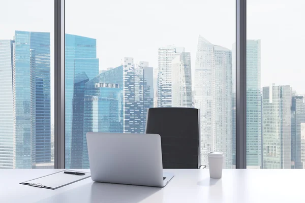 A workplace in a modern panoramic office with Singapore view. A white table, black leather chair. Laptop, writing pad for notes and a cap of coffee are on the table. Office interior. 3D rendering.