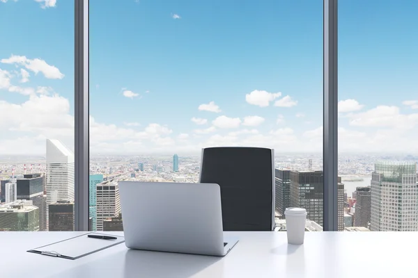 A workplace in a modern panoramic office with New York City view. A white table, black leather chair. Laptop, writing pad for notes and a cap of coffee are on the table. Office interior. 3D rendering.