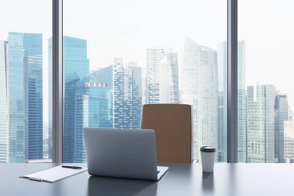 A workplace in a modern panoramic office with Singapore view. A grey table, brown leather chair. Laptop, writing pad for notes and a cap of coffee are on the table. Office interior. 3D rendering.