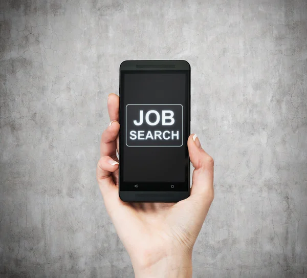 A hand holds a fancy smartphone. Words: \' Job search \' on the screen. A concept of recruitment. Concrete background.