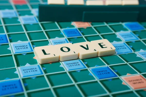 The word 'LOVE' is made of the scrabble tiles. Scrabble game board as a background.