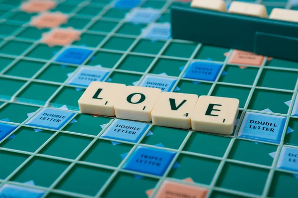 The word \'LOVE\' is made of the scrabble tiles. Scrabble game board as a background.