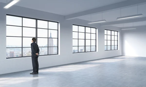 A full length man in formal suit who is looking out the window, New York panoramic view. A modern loft style open space.