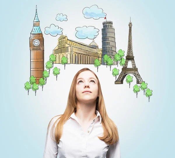 A beautiful woman is looking up by dreaming about the visiting of the most famous European cities. The concept of tourism and sightseeing. Light blue background.