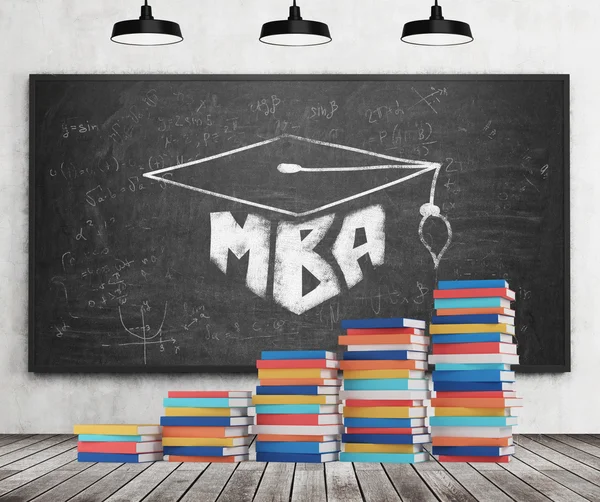 A stair is made of colourful books. A graduation hat is drawn on the black chalkboard. MBA concept. Concrete wall, wooden floor and three black ceiling lights.