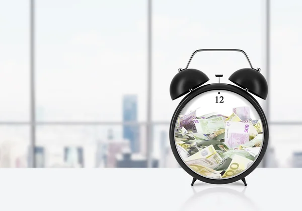 There is EURO bills inside the alarm clock which is on the table. The concept of \'time is money\' and a time management. Panoramic New York office background.