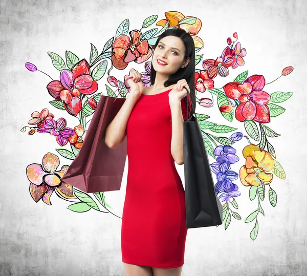 A happy brunette woman holds colourful bags from fancy shops. The concept of shopping. A sketch of different flowers is drawn on the concrete wall.