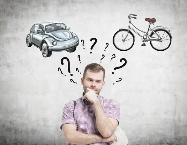 A handsome man is trying to chose the most suitable way for travelling or commuting. Two sketches of a car and a bicycle are drawn on the concrete wall. Question marks are around man\'s head.