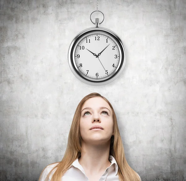 A portrait of a beautiful lady who is looking at the hovering pocket watch. A concept of a value of time in business. Concrete background.