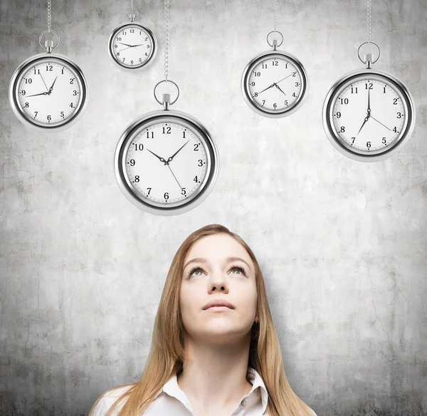 A portrait of a beautiful lady who is looking at the hovering pocket watches. A concept of a value of time in business. Concrete background.