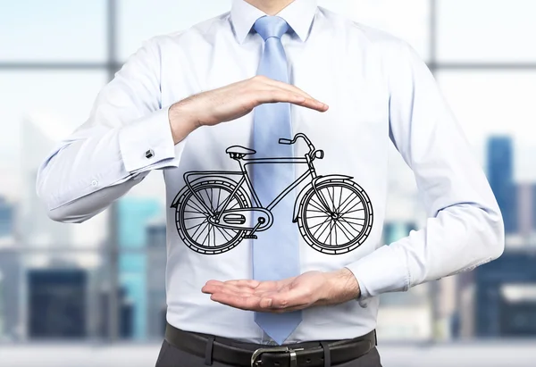 A person in formal clothes holds a sketched bicycle between his hands. A modern panoramic office in blur is on the background. A concept of environmental friendly ways of commuting and travelling.