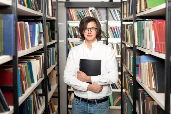 Young man with dark hair standing and holding a black copy book