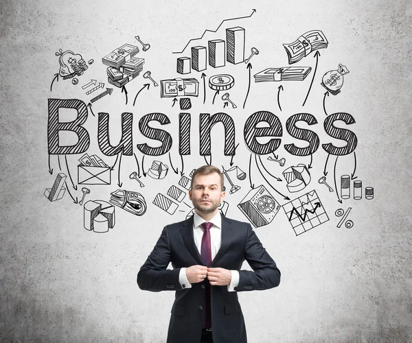 A young businessman standing and buttoning up his jacket, the word 'business' and numerous business symbols over his head. Concrete background. Concept of developing a business.