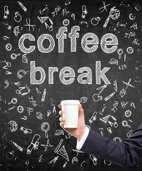 A hand in a black suit holding a paper cup. \'Coffee break\' written over it. Black background with different scientific symbols. Concept of coffee break.