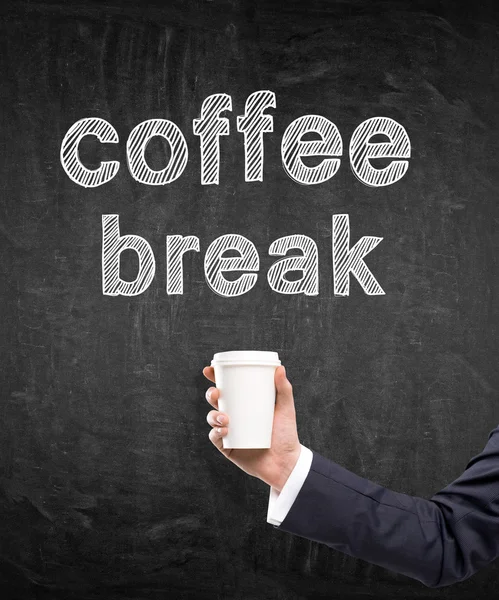 A hand in a black suit holding a paper cup. 'Coffee break' written over it. Black background. Concept of coffee break.