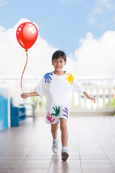 Little boy running at school with happy face taking a red balloon