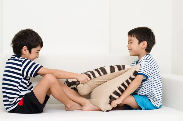 Little sibling boy playing pillow fighting on sofa