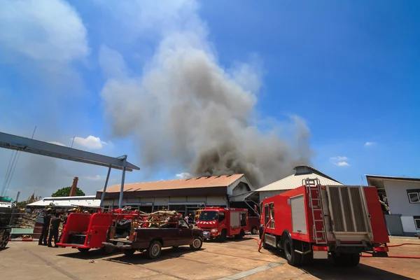 Fire truck and burning warehouses with black smoke against blue