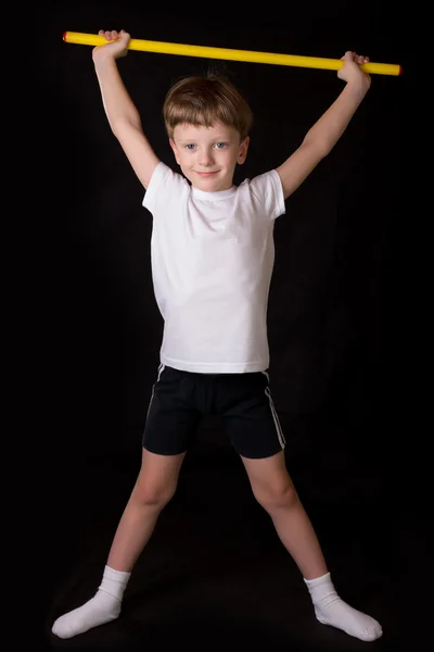 Boy athlete performs exercises with gymnastic stick in the gym