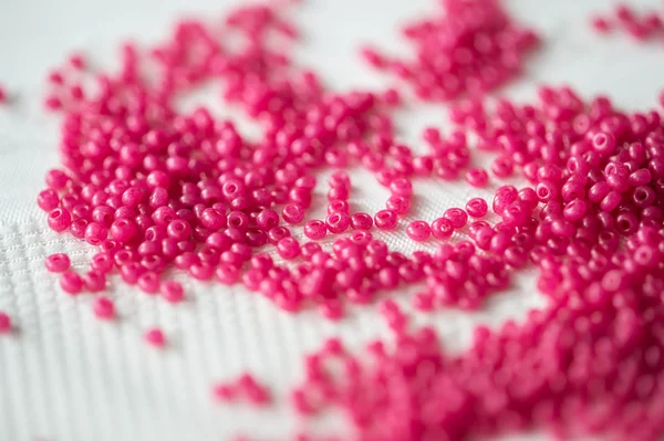Seed beads of crimson color on the textile background close up