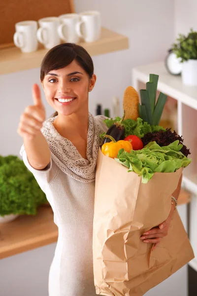 Young woman holding grocery shopping bag with vegetables Standing in the kitchen and showing ok