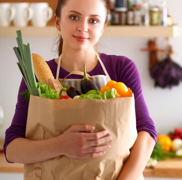 Young woman holding grocery shopping bag with vegetables Standing in the kitchen