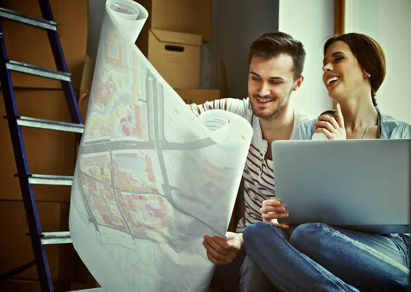 Young couple sitting on the floor and looking at the blueprint of new home