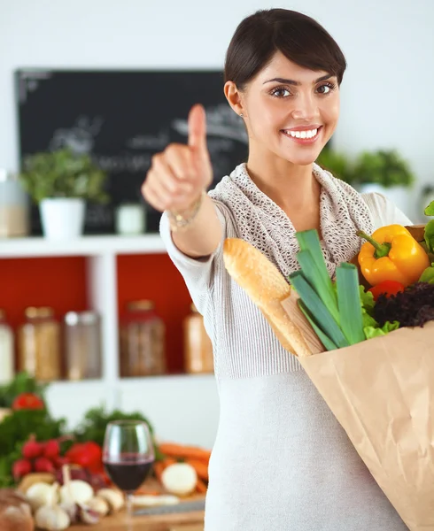 Young woman holding grocery shopping bag with vegetables Standing in the kitchen and showing ok