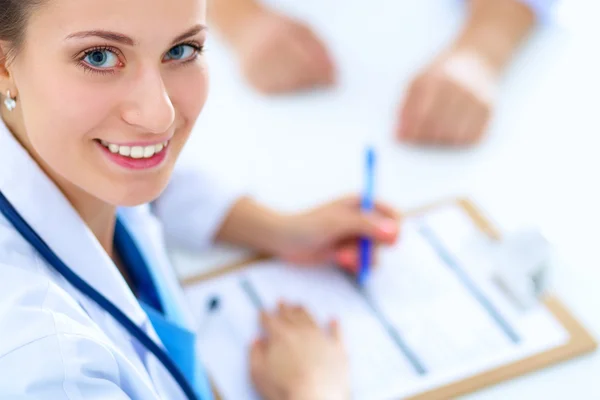 Closeup of beautiful female doctor filling in a form with colleague in background.