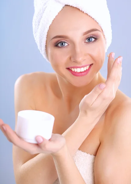 Beautiful young woman applying a creme on her face isolated on gray background