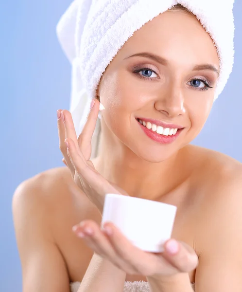 Beautiful young woman applying a creme on her face isolated on gray background