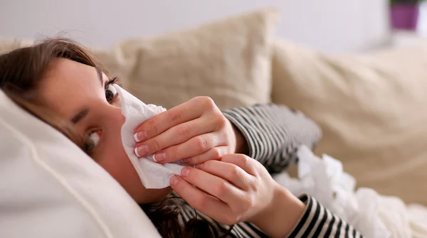 Portrait of a sick woman blowing her nose while sitting on the sofa