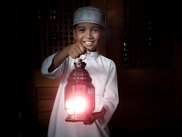 Muslim child in traditional white dress holding lantern