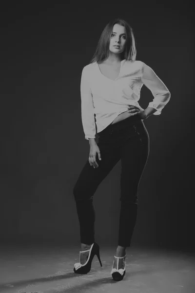 Stylishly dressed young business lady. The image of a beautiful young business lady. Girl in black pants and a white shirt on a dark background. Photo for fashion and social magazines, websites.