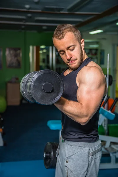 Man at the gym. Man makes exercises dumbbells. Sport, power, dumbbells, tension, exercise - the concept of a healthy lifestyle. Article about fitness and sports.