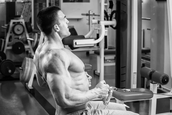 Strong muscular man doing exercises in the gym. Beautiful body on a black and white photo. Healthy lifestyle.