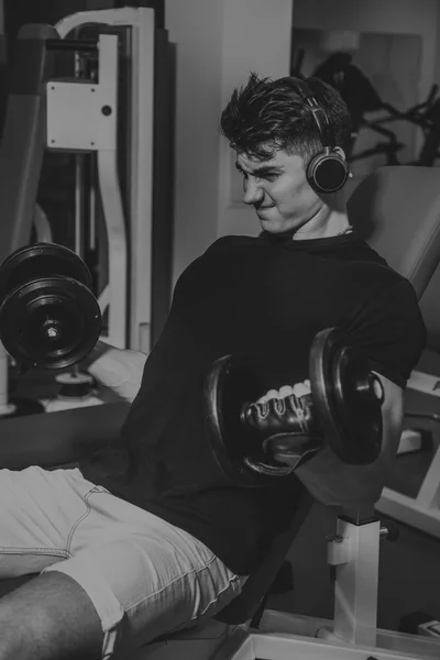 Man at the gym. Man makes exercises dumbbells. Sport, power, dumbbells, tension, exercise - the concept of a healthy lifestyle. Article about fitness and sports.