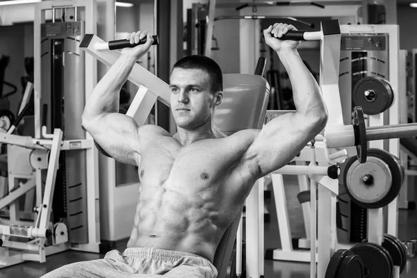 Strong muscular man doing exercises in the gym. Beautiful body on a black and white photo. Healthy lifestyle.