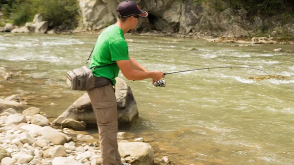 Sportsman fisherman shows catch trout in a mountain river. Interesting and hazardous confrontation between fishermen and fish. Healthy and emotional rest on a mountain river. Photo fishing magazines